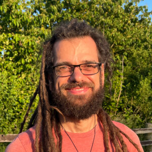 Profilbild von Petros Sofocli ein Executive virtueller Assistent und Accountability Partner im Sonnenuntergang mit roten T-shirt und grünen Hintergrund - MovingVA